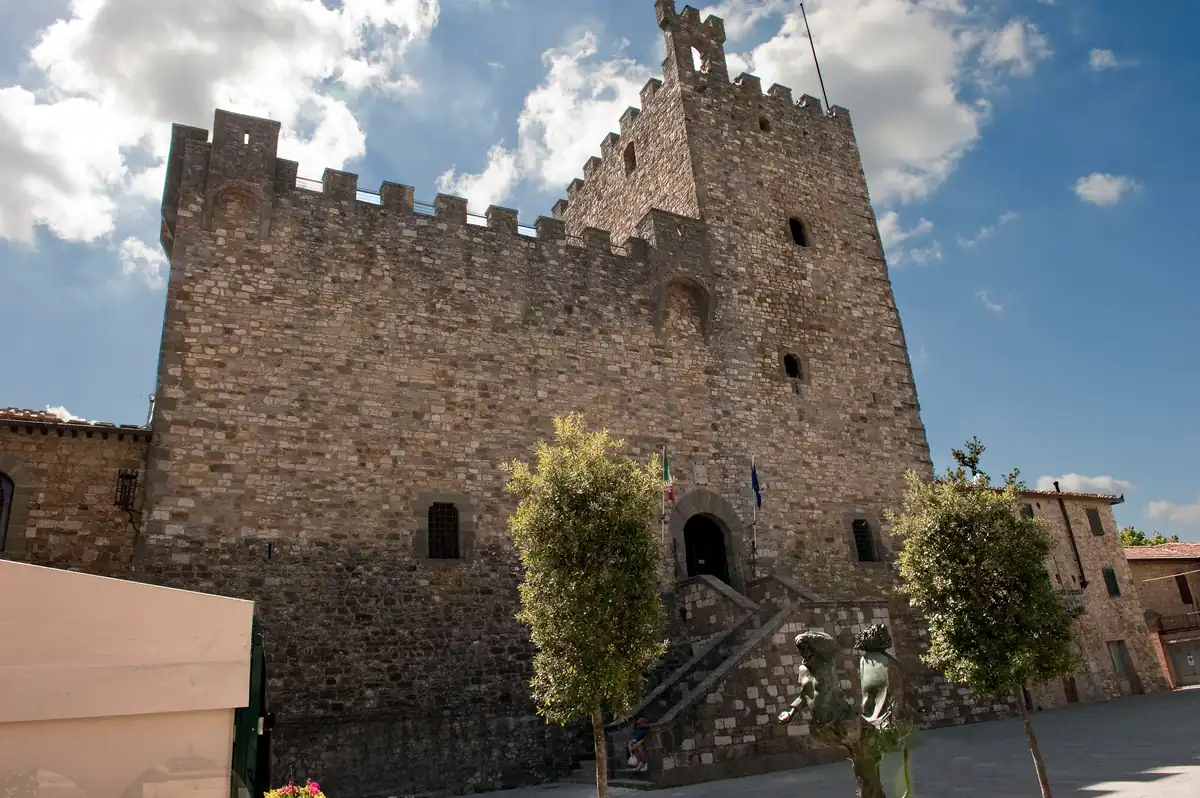 Veduta dal basso della Rocca di Castellina in Chianti, con mura merlate in pietra e cielo nuvoloso.