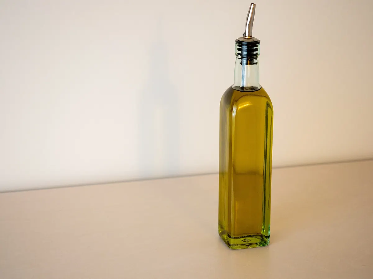 Bottiglia di olio extravergine d'oliva su superficie chiara con beccuccio dosatore