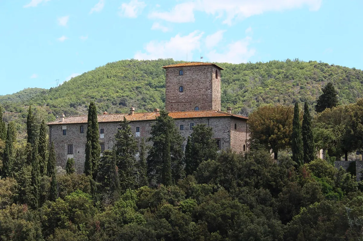 Castello di Mugnana in pietra con torre, tra cipressi e bosco collinare