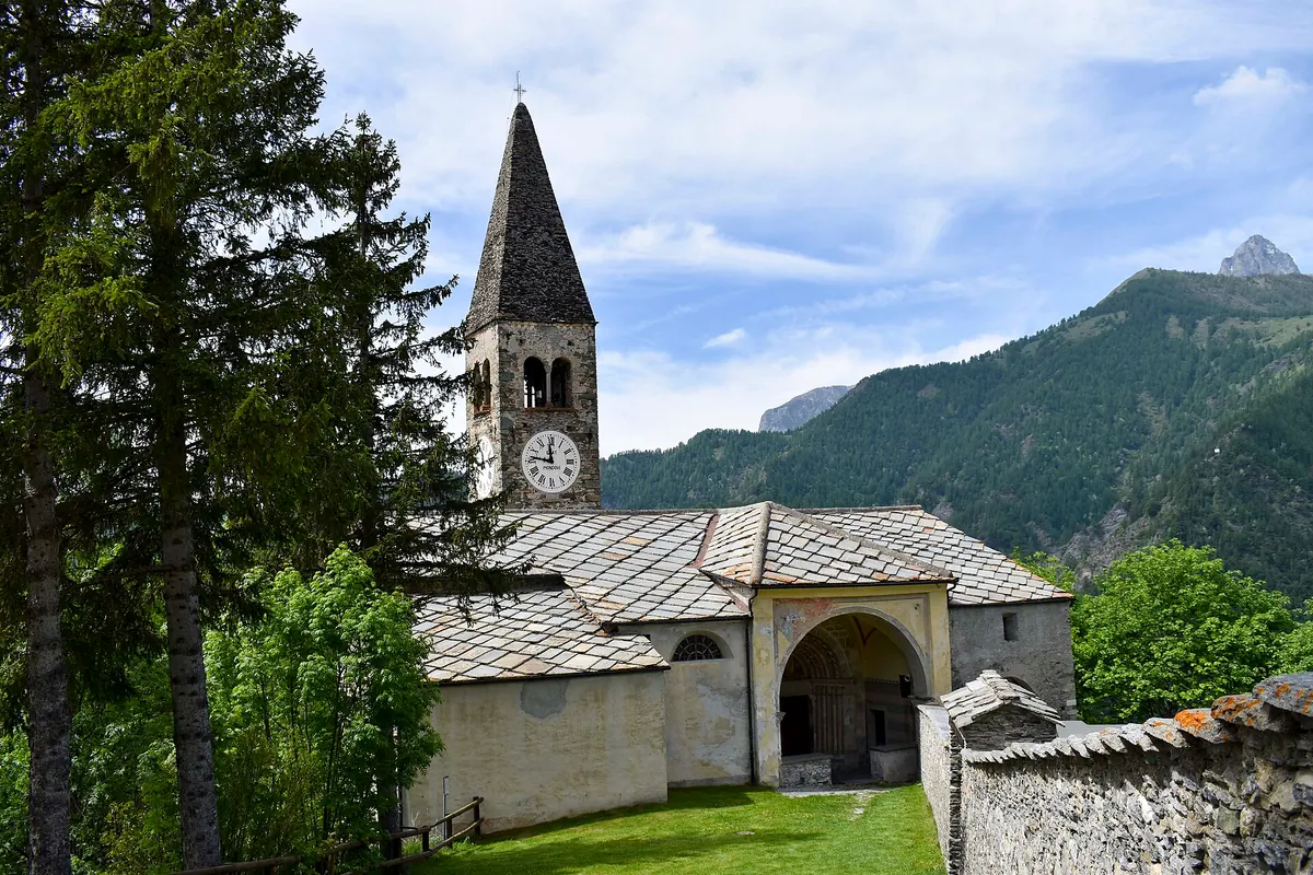 Chiesa parrocchiale con campanile in pietra tra alberi e montagne