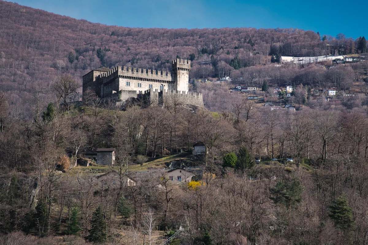 Castello fortificato su un colle boscoso, visto da lontano con torre e mura merlate