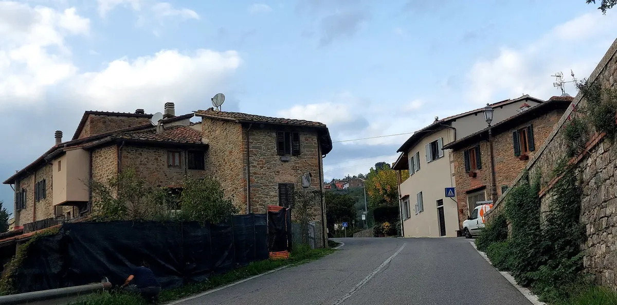 Strada in salita tra case in pietra nel Chianti, con cielo nuvoloso