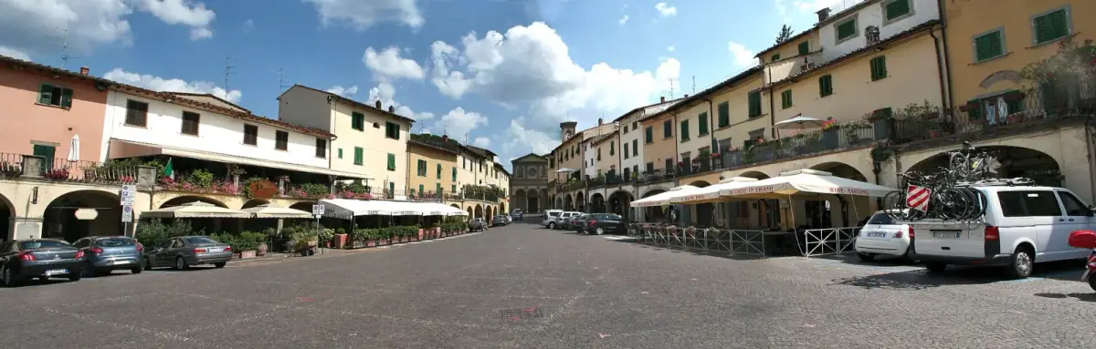 Piazza Matteotti a Greve in Chianti con portici, tavolini dei caffe e auto parcheggiate