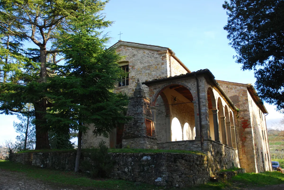 Oratorio in pietra con portico ad archi, immerso tra alberi, visto da terra