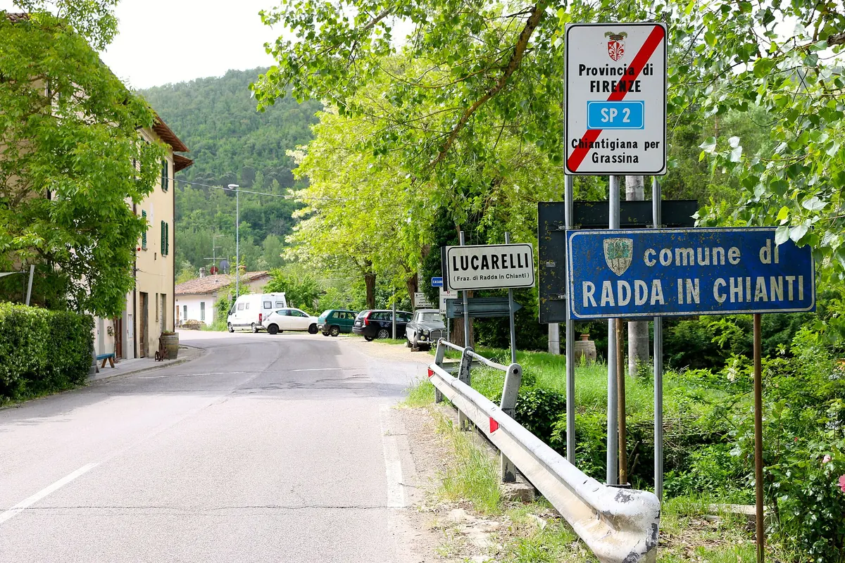 Ingresso di Lucarelli con cartelli stradali lungo una strada alberata a Radda in Chianti