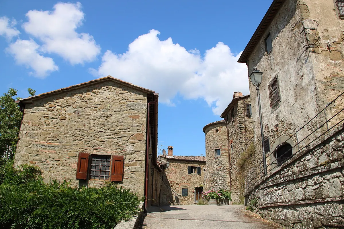 Vicolo di Volpaia tra case in pietra e torretta, sotto un cielo azzurro con nuvole